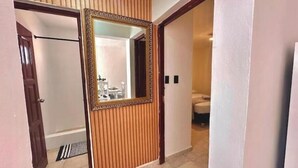 Ein Flur mit einer Holztür, einem Spiegel und Blick in ein Badezimmer mit Toilette und Waschbecken.