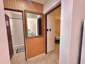 A hallway with a wooden door, a mirror, and a view into a bathroom with a toilet and sink. - Downtown Apartment (Santo Domingo)
