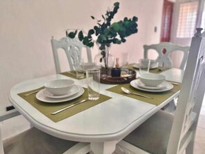 A dining table set with white plates, bowls, and cutlery, accompanied by a green placemat. - Downtown Apartment (Santo Domingo)
