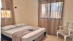 Ein Schlafzimmer mit einem Bett, einem Sessel und einem Fenster mit Vorhängen.