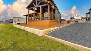 A modern building with a wooden deck and a covered area, surrounded by a gravel area and grass. - Inviting Tiny Home Retreat with Resort-Style Amenities Near Fredericksburg, TX (Fredericksburg)