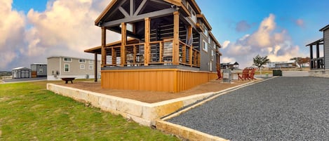 A modern building with a wooden deck and a covered area, surrounded by a gravel area and grass.