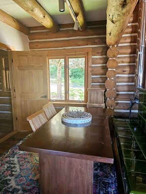A wooden dining table with chairs, a window with a view of greenery, and a log wall. - Luxury Montana-Style Log Estate with Private Vineyard & Spa Near Purcellville, VA (Purcellville)