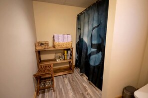 A bathroom with a wooden shelf unit, a small stool, a trash bin, and a blue curtain with a face design. - Luxury Montana-Style Log Estate with Private Vineyard & Spa Near Purcellville, VA (Purcellville)