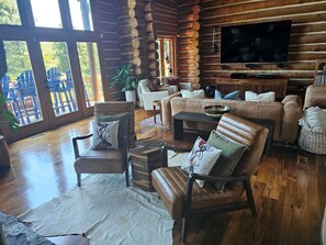 A log cabin interior with a large TV, leather furniture, and a wooden floor.