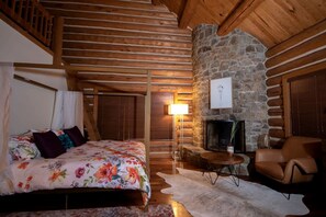 Um quarto de cabana de registos acolhedor com uma cama, lareira, uma poltrona e uma parede de pedra.