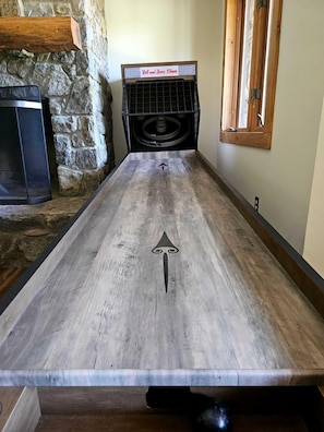 A long, narrow wooden table with a central arrow design, a stone wall, a fireplace, and a speaker on a stand.