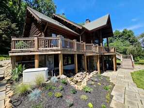 A two-story log cabin with a deck and a stone pathway leading to the entrance.