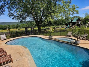 A swimming pool with a curved design, surrounded by a fence, and equipped with lounge chairs and a small deck area.