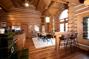 Interior de uma cabana de tronco com cozinha, sala de jantar e uma grande janela.