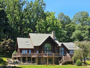 A log cabin with a balcony, a chimney, and a stone foundation.