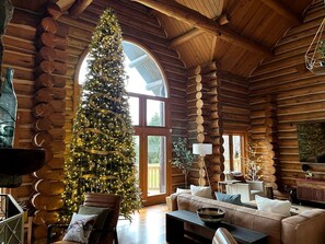 A log cabin interior with a large Christmas tree, a sofa, and a dining table.