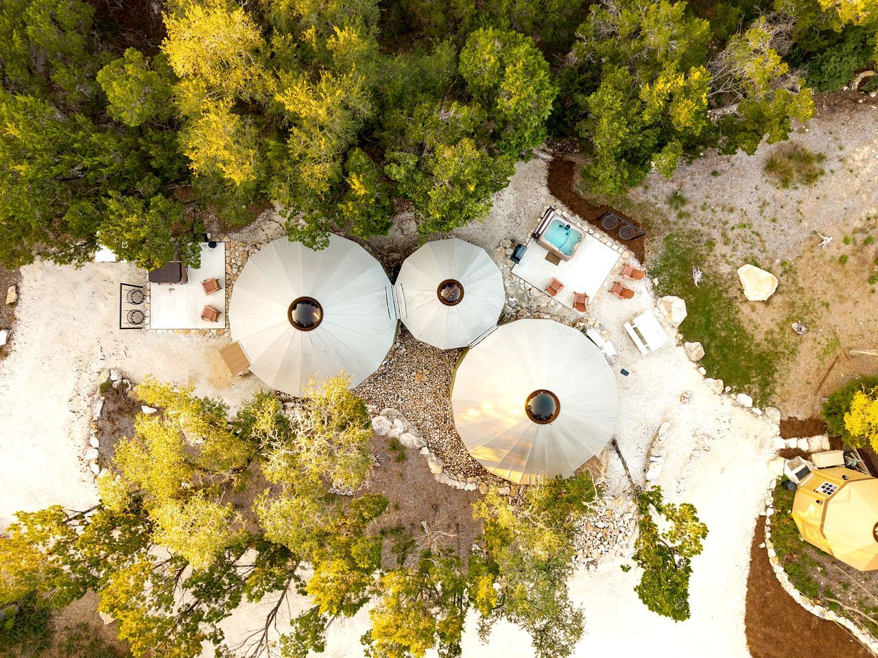 An aerial view of a campsite with three large white tents, a swimming pool, and surrounding trees.