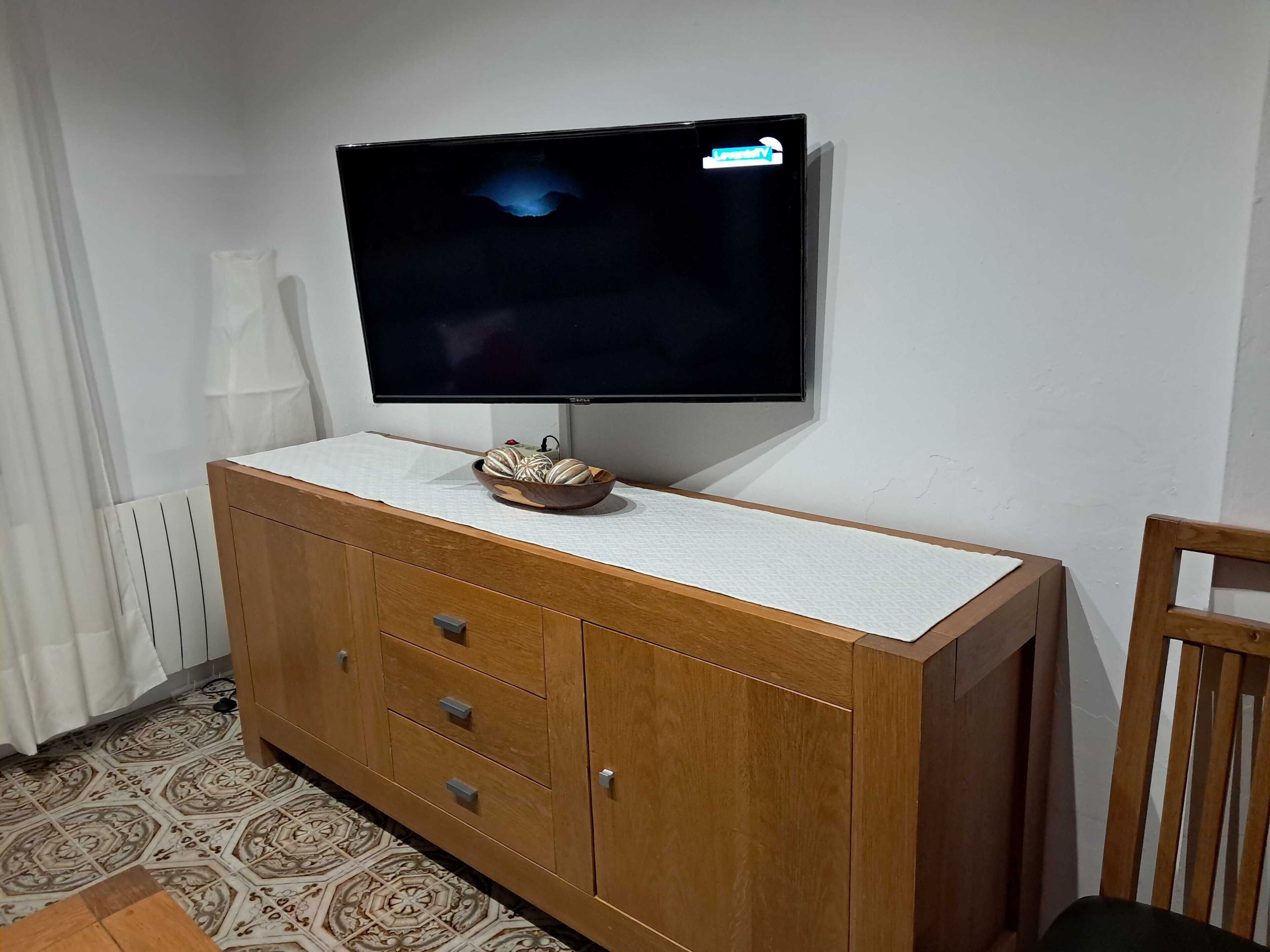 Un téléviseur fixé au mur, au-dessus d’un meuble en bois doté de tiroirs.