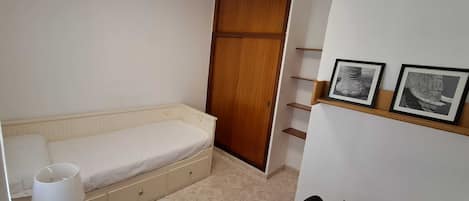A bedroom with a bed, bedside table, lamp, and a wooden wardrobe.