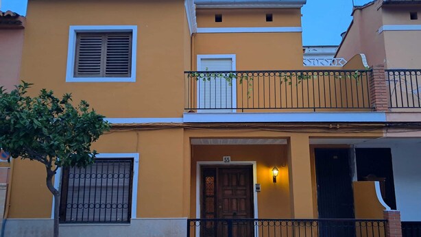 Un edificio a due piani con un balcone, una porta con un numero e un piccolo albero di fronte.