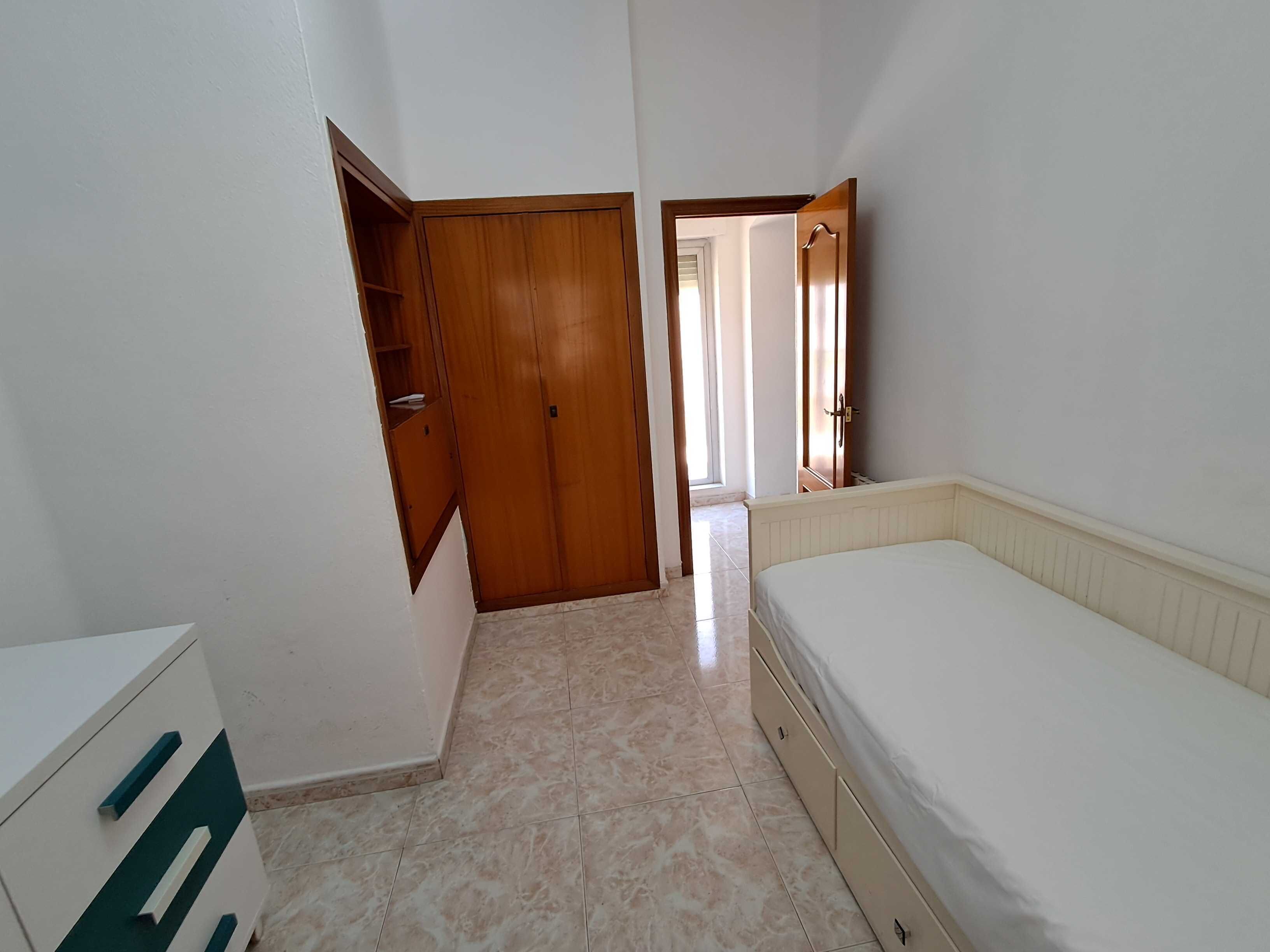 Een slaapkamer met een bed, een kledingkast en een deur naar een andere kamer.