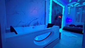 Een moderne badkamer met een ruime badkuip, een spiegel en een muur met een geometrisch patroon.