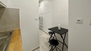 Een smalle gang met een kleine tafel, twee stoelen, een witte muur en een radiator.