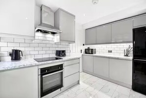 A modern kitchen with white cabinetry, a built-in oven, a microwave, and a kettle. - Sleeps5-freeparking-familyfriendly-5mintostation (London)