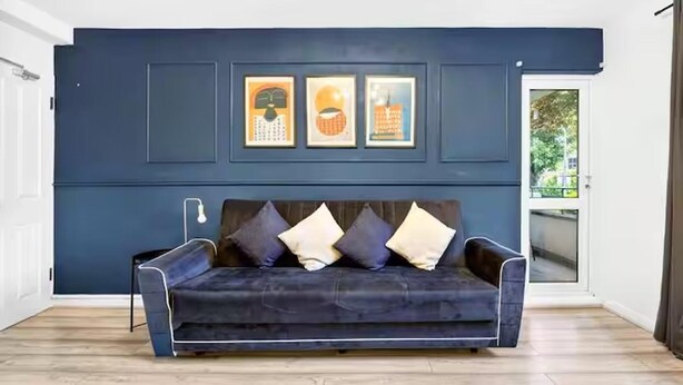 A dark blue sofa with four cushions in a room with wooden flooring and a white door. - Sleeps5-freeparking-familyfriendly-5mintostation (London)