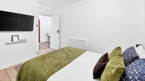 A bedroom with a bed, pillows, a TV mounted on the wall, and a door leading to another room. - Sleeps5-freeparking-familyfriendly-5mintostation (London)