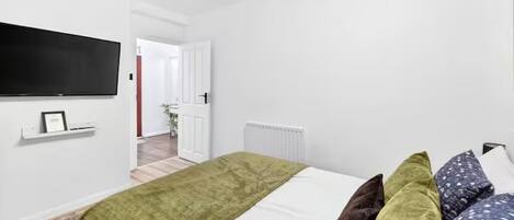 A bedroom with a bed, pillows, a TV mounted on the wall, and a door leading to another room.