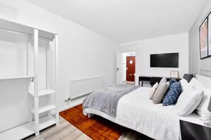 A modern bedroom with a bed, a wardrobe, a radiator, a television, and a door leading to another room. - Sleeps5-freeparking-familyfriendly-5mintostation (London)