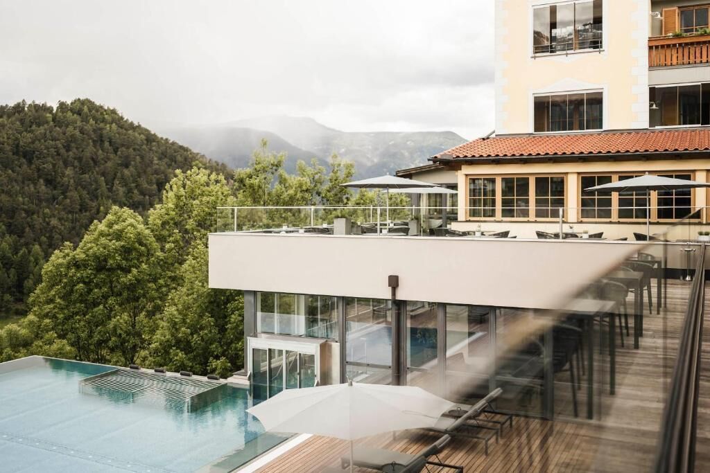 Zona de piscina en la azotea con sillones de descanso y sombrillas, con vista a una ladera boscosa.