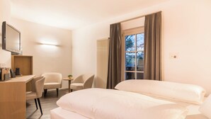 A hotel room with a bed, a desk, a chair, and a television. - Hotel Alpenflora (Castelrotto)