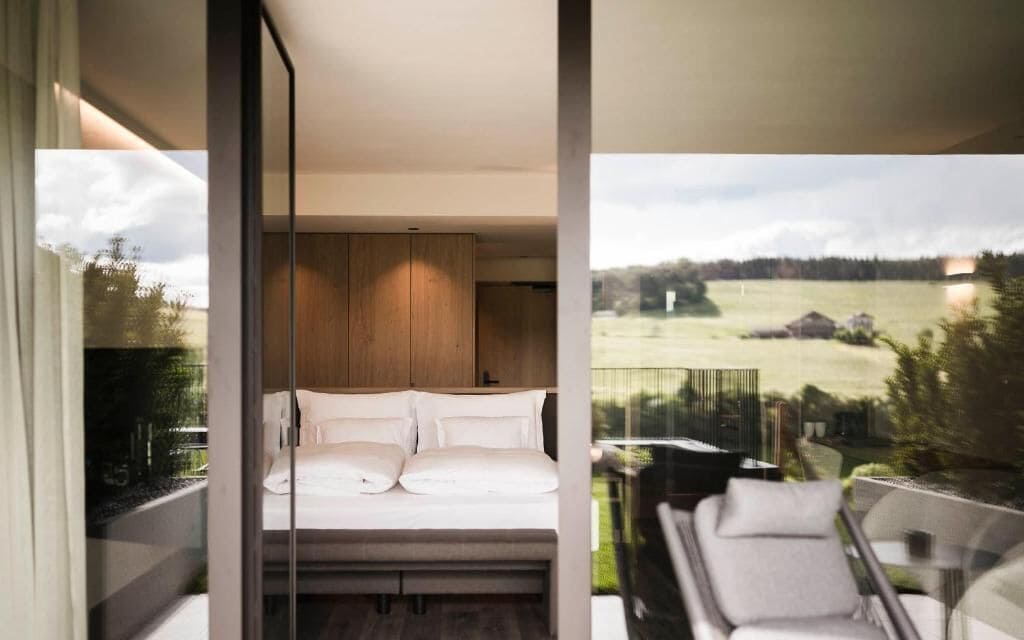 Un dormitorio moderno con una cama grande, paneles de madera y un balcón con mobiliario exterior.