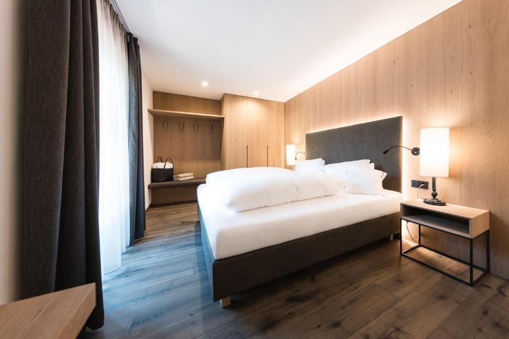 A modern hotel room with a large bed, a bedside table with a lamp, and a wardrobe.