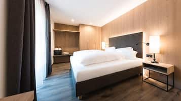 A modern hotel room with a large bed, a bedside table with a lamp, and a wardrobe.