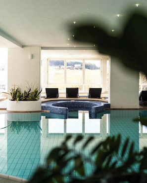 An indoor swimming pool with a view of a rural landscape through large windows. - Hotel Alpenflora (Castelrotto)