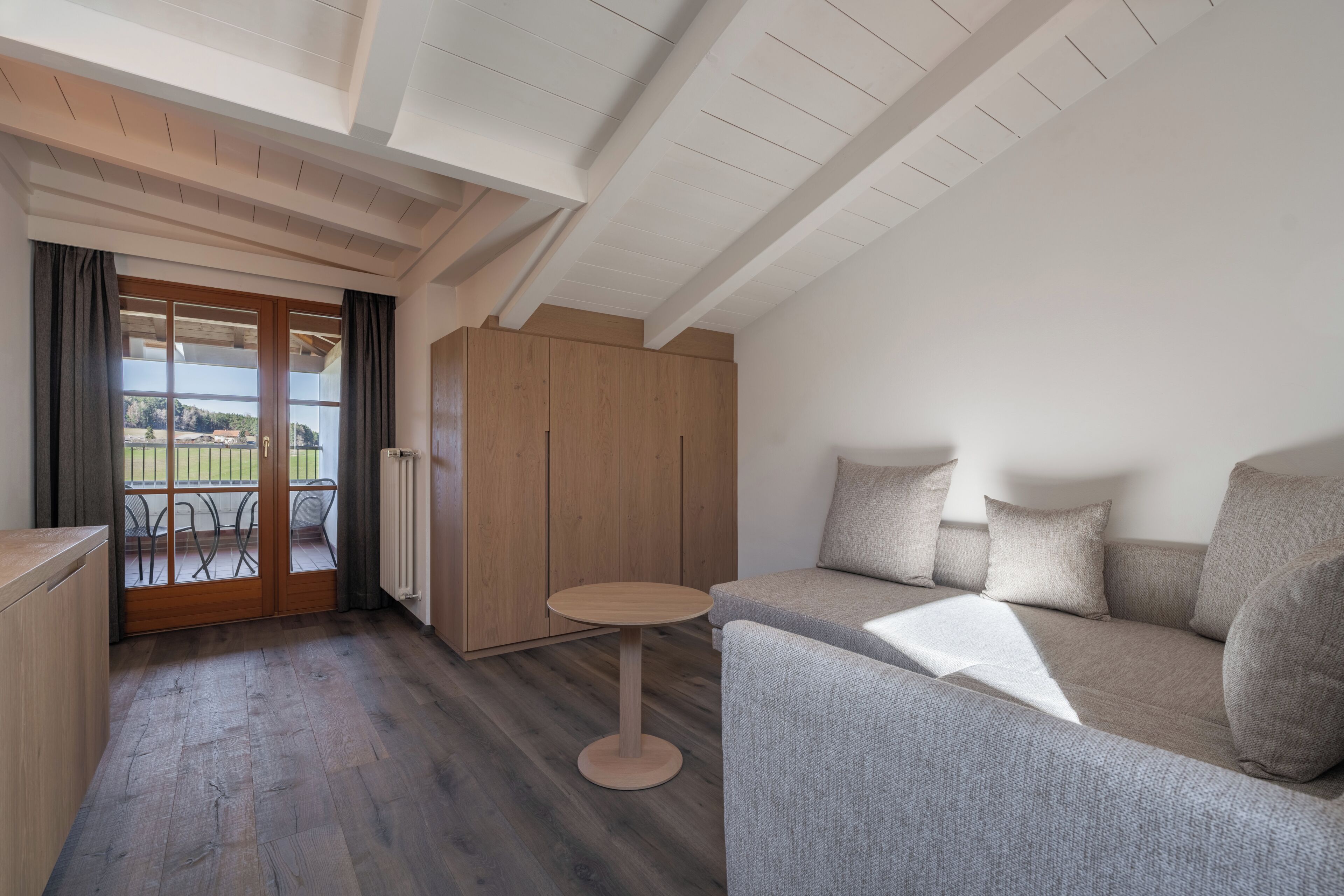 A modern interior with a wooden floor, a grey sofa, a small round table, and a wooden wardrobe.
