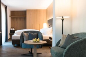 A hotel room with a bed, a round table with fruit, a sofa, and a lamp.
