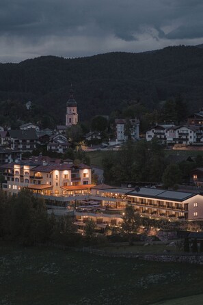A town with a prominent church tower, a modern hotel with multiple floors, and surrounding residential buildings. - Hotel Alpenflora (Castelrotto)