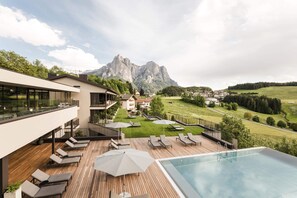 A modern outdoor pool area with lounge chairs and umbrellas, overlooking a mountainous landscape. - Hotel Alpenflora (Castelrotto)