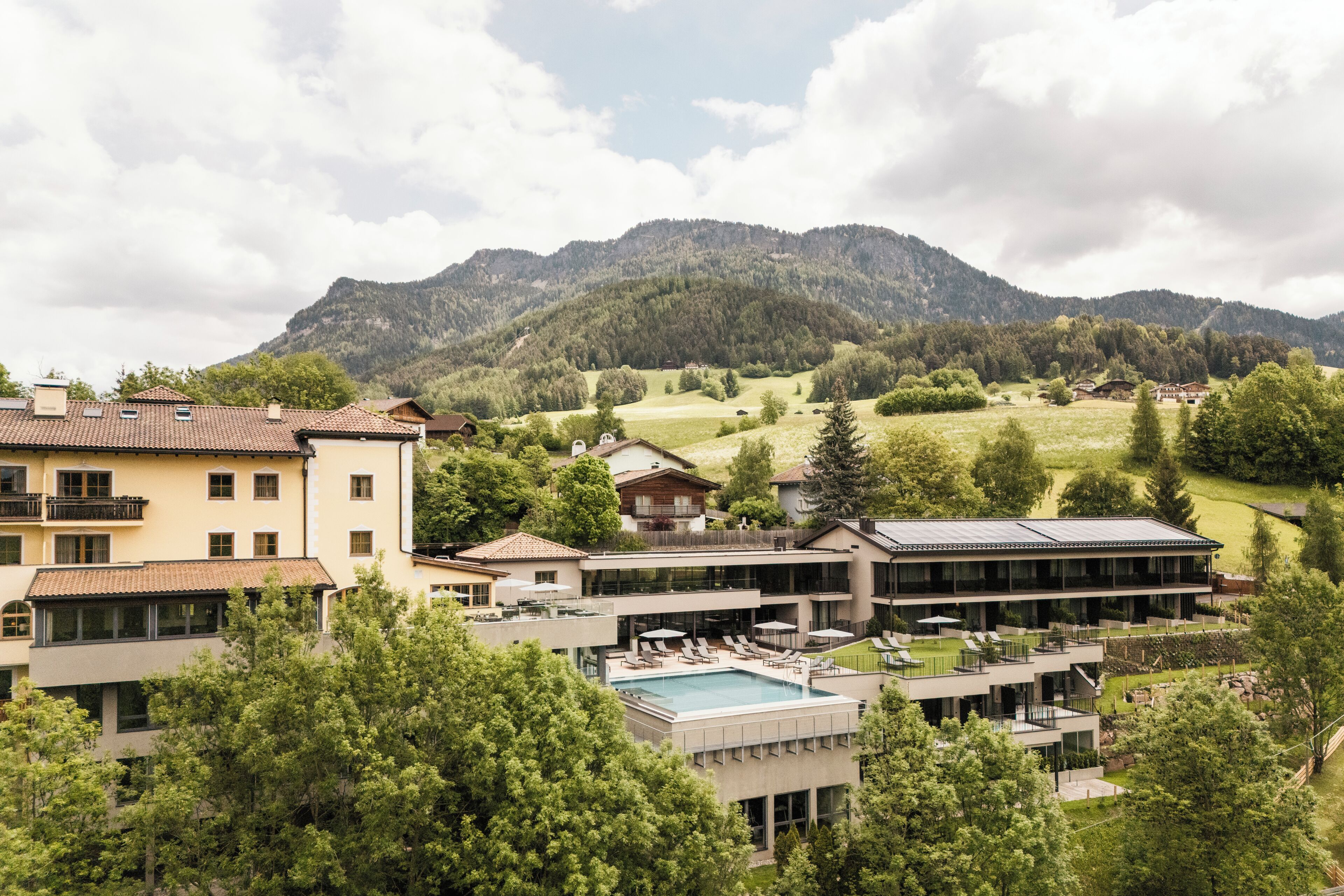 A hotel with multiple buildings, a swimming pool, and a mountainous backdrop.