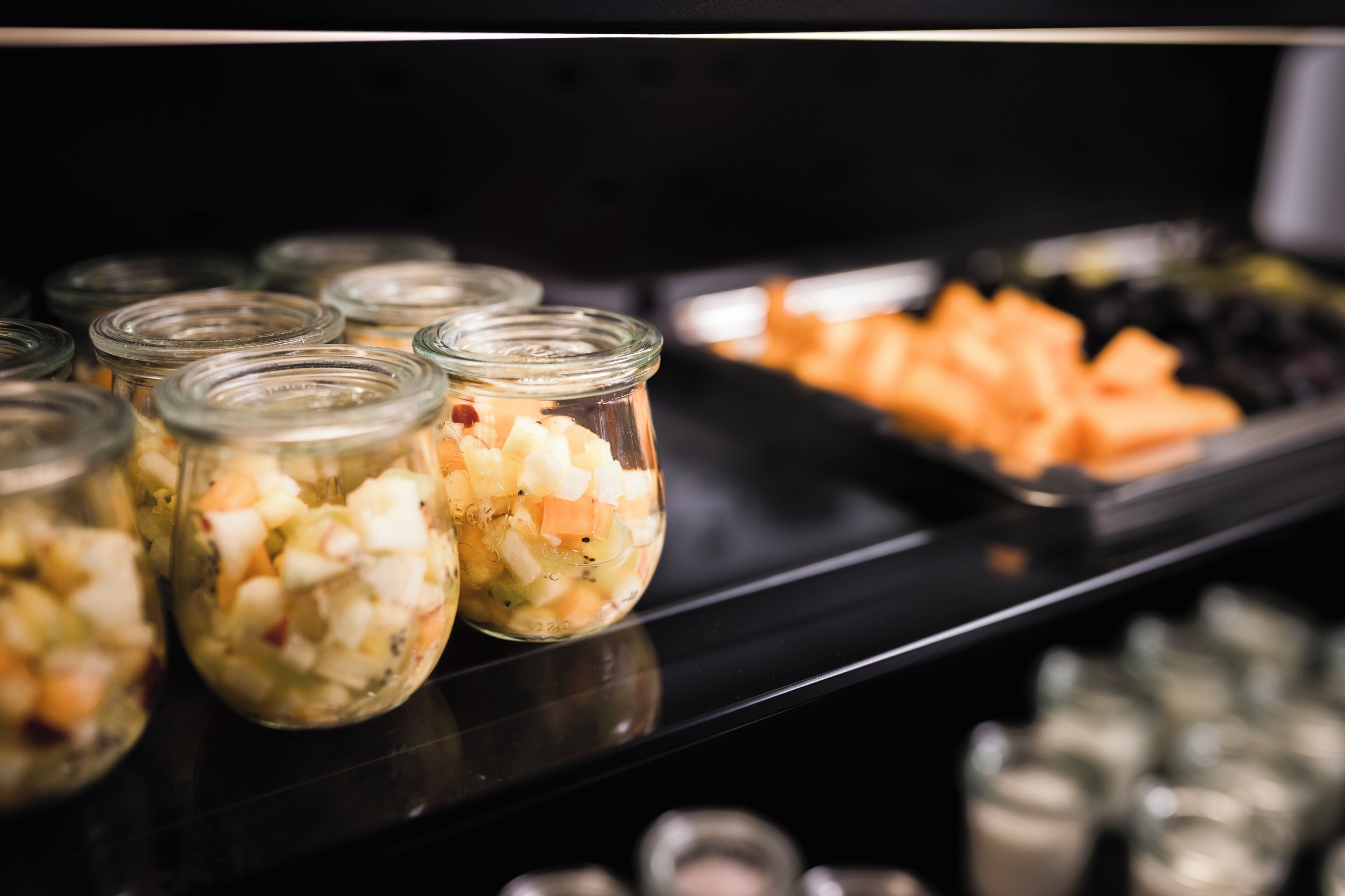 Un buffet proposant une variété de plats, notamment des pots de salade de fruits mélangés et un plateau de fruits coupés.