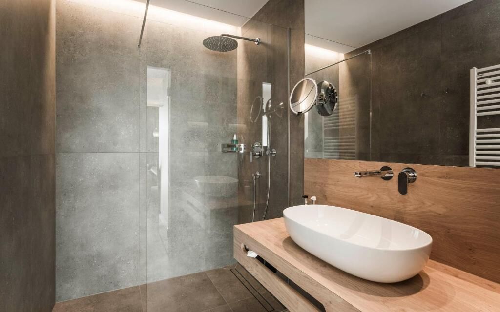Ein modernes Badezimmer mit einem großen Spiegel, einem Holzwaschtisch und einer gläsernen Dusche.
