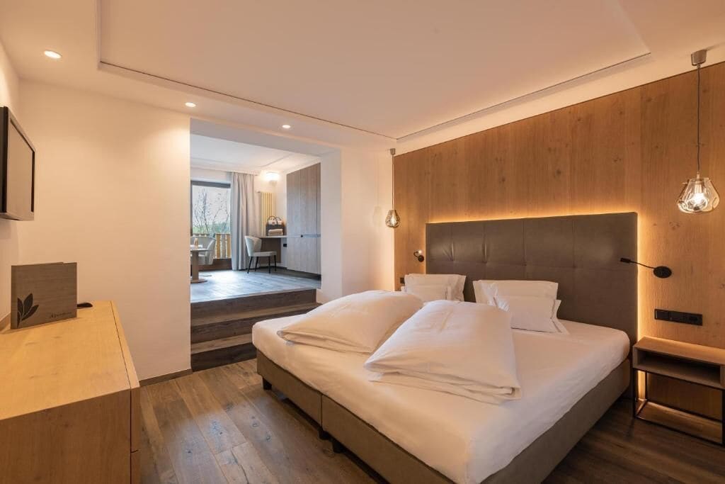 Quarto moderno com cama grande, painéis de madeira na parede e vista para outro ambiente.