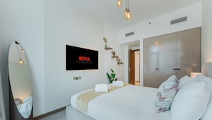 A modern hotel room with a large bed, a flat-screen TV, a mirror, and a wardrobe. - PVH - Urban Oasis by Missoni - 1BR (Dubai)