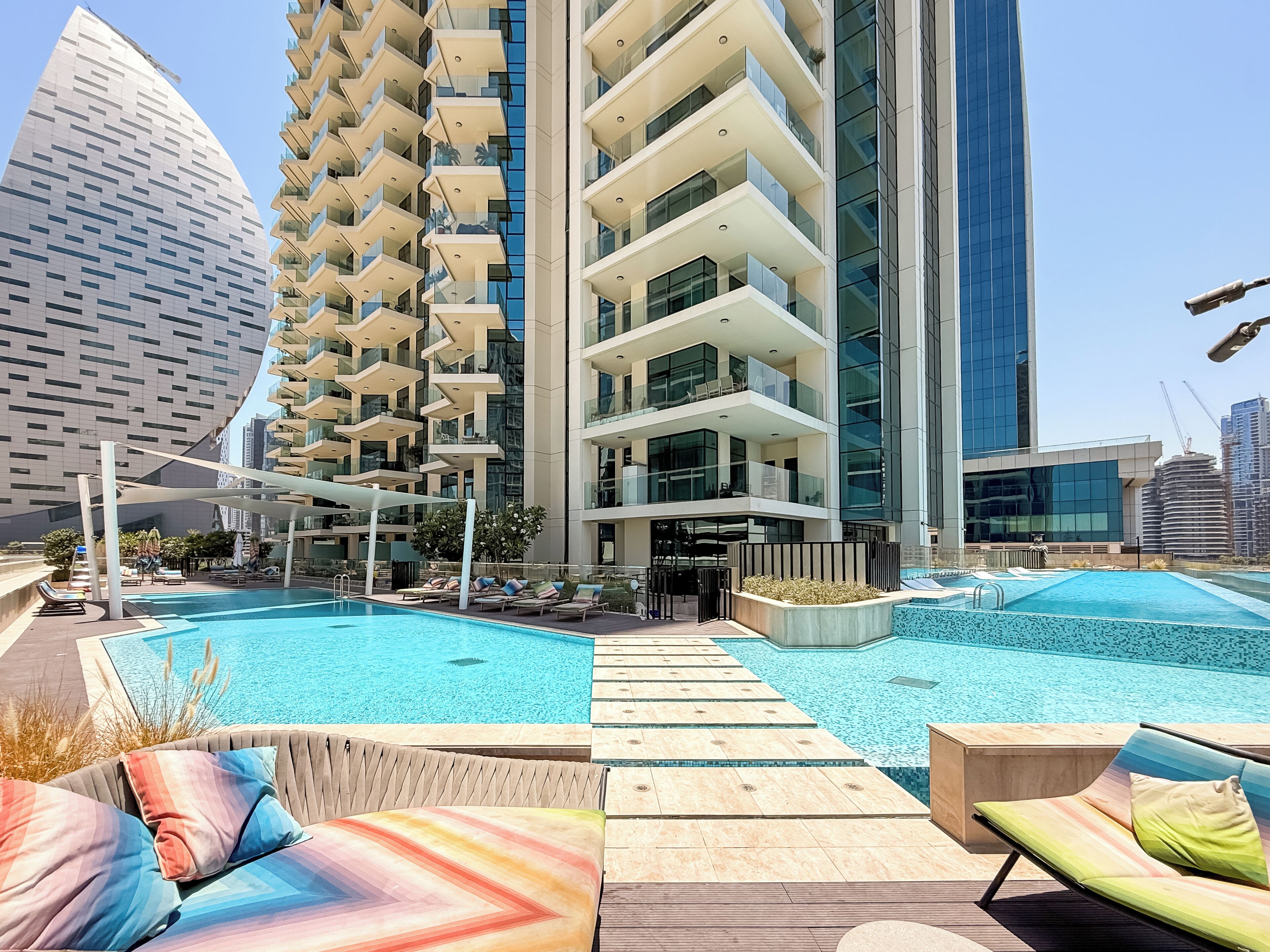 A modern hotel with a rooftop pool, lounge chairs, and a view of surrounding high-rise buildings.