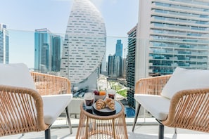 Ein Balkon mit Korbstühlen, einem Tisch mit Croissants, Obst und Getränken sowie Blick auf die Stadt.