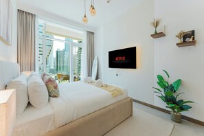 A modern hotel room with a large bed, a TV mounted on the wall, a city view, and a potted plant. - PVH - Urban Oasis by Missoni - 1BR (Dubai)