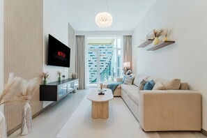 A modern living room with a flat-screen TV, a sofa, a coffee table, and a view of a cityscape through large windows. - PVH - Urban Oasis by Missoni - 1BR (Dubai)