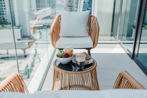 A balcony with wicker furniture, a glass table, and a bowl of fruit and pastries. - PVH - Urban Oasis by Missoni - 1BR (Dubai)