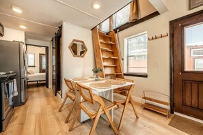 Una cocina con una mesa de madera, sillas, un refrigerador y una escalera.