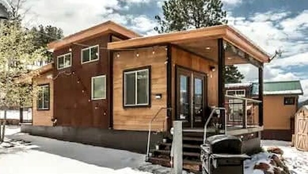 A modern wooden cabin with a covered porch, large windows, and a snow-covered ground. - Beautiful Tiny Home Nestled in Woodland Park and near Manitou Springs, Perfect for a Weekend Getaway (Woodland Park)